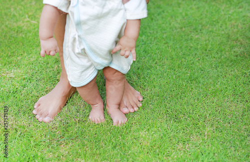 Close up infant baby feet learning to walk with his mother on the green grass. First steps.