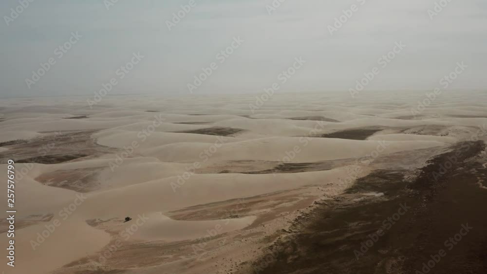 Aerial: A truck with kitesurfers traveling through the dunes of Lencois Maranhenses in Brazil, during dry season. Aerial: A truck with kitesurfers traveling through the dunes of Lencois Maranhenses in Brazil, during dry season.