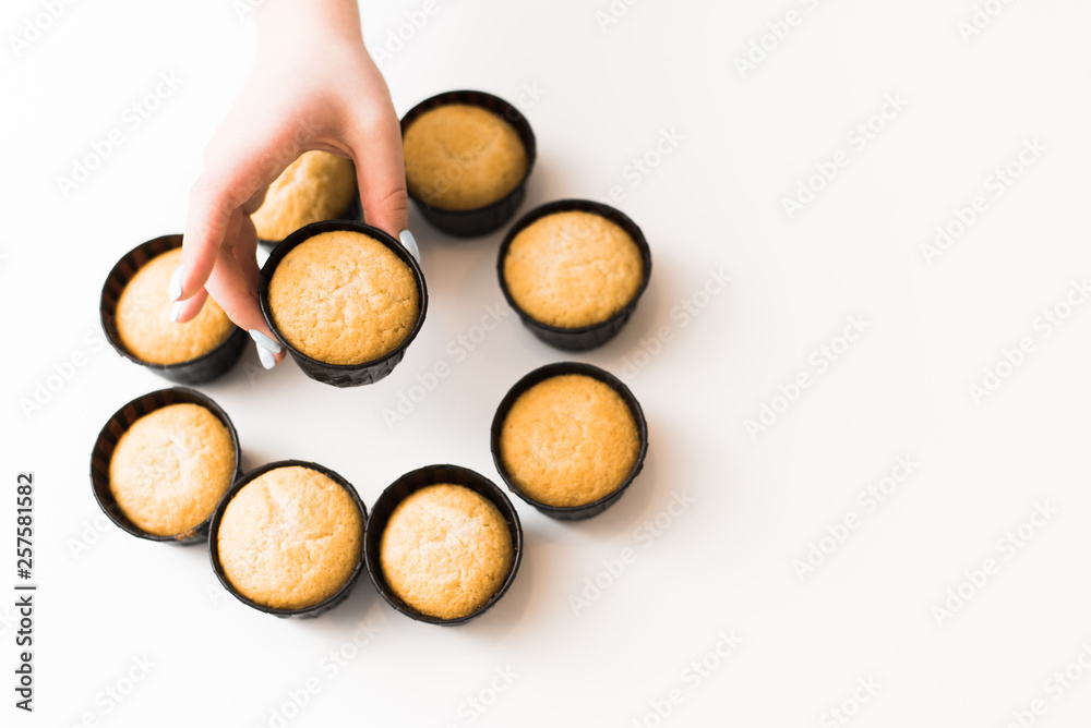 Fototapeta premium cupcakes without cream on a white background with a place for the text. The girl takes a cupcake from a pile of sweets. copyspace