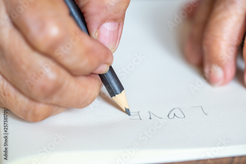 Senior woman's right Hand writing " Love " on ivory paper background, Close up & Macro shot, Selective focus, Stationery concept