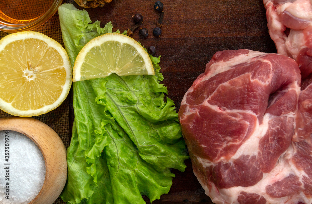 Pork meat, source of protein. Raw pork steak. On a cutting board, on a wooden table. With spices, herbs and lemon for cooking. Copy space on top. Pork meat, source of protein. Raw pork steak. On a cutting board, on a wooden table. With spices, herbs and lemon for cooking. Copy space on top.