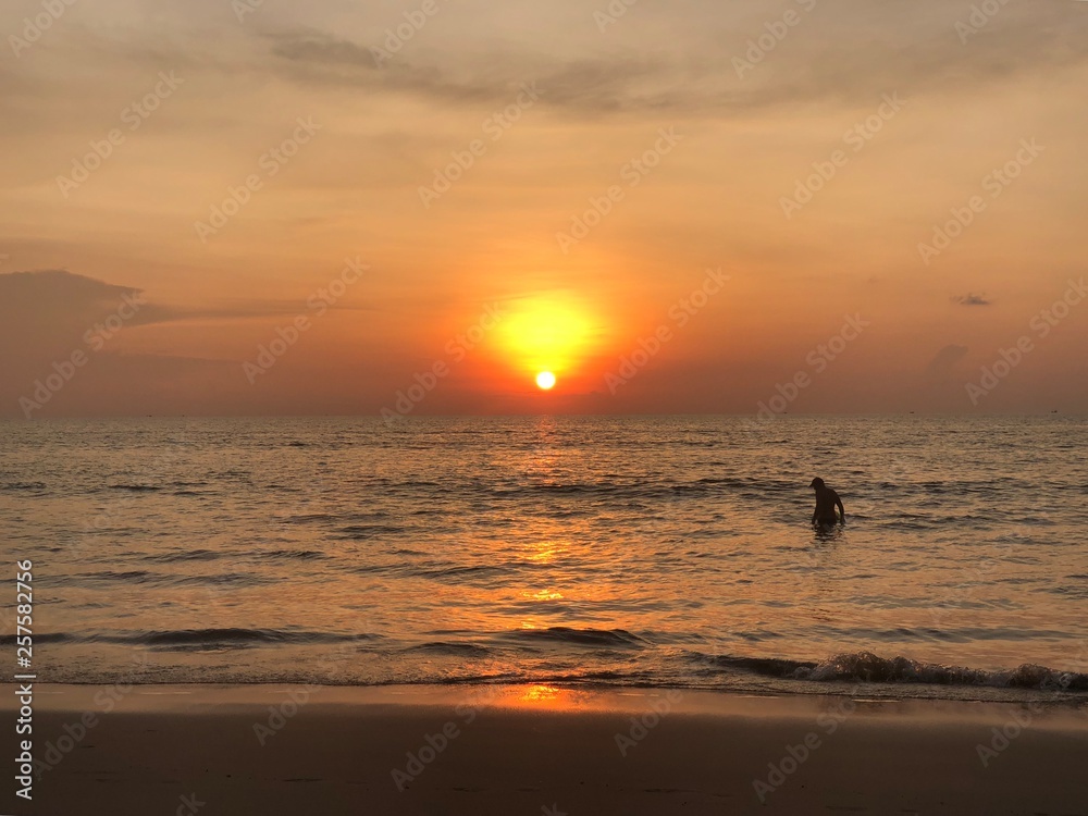the sun sets on the horizon where the sea joins the sky. people-adult and child-swim in the sea and enjoy the Golden sunset on the beach