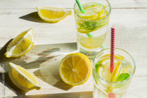 glass of homemade lemonade with lemons, mint and paper straws on wooden rustic background. Summer refreshing beverage. hard shadows