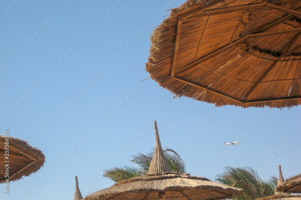 straw canopy on the beach with flying aircraft
