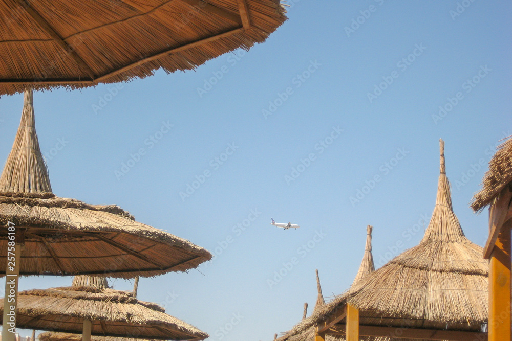 straw canopy on the beach with flying aircraft
