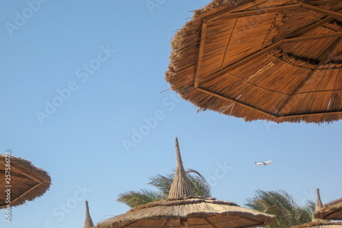 Obraz na płótnie straw canopy on the beach with flying aircraft w salonie