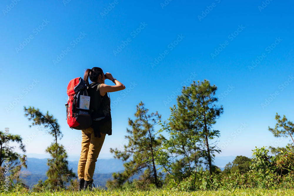 Hiker woman look binoculars on the mountain, background blue sky Hiker woman look binoculars on the mountain, background blue sky