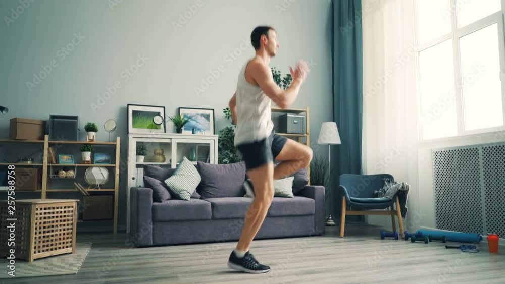 Professional runner is exercising at home running on the spot doing cardio training wearing sneakers and sports clothing. Sportive people, house and healthy hobby concept. Professional runner is exercising at home running on the spot doing cardio training wearing sneakers and sports clothing. Sportive people, house and healthy hobby concept.