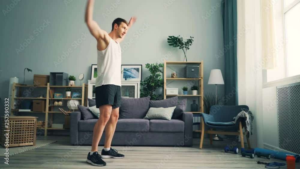 Good-looking sportsman in stylish sportswear is exercising at home rotating arms doing physical exercises for shoulders and chest muscles. House and wellness concept.
