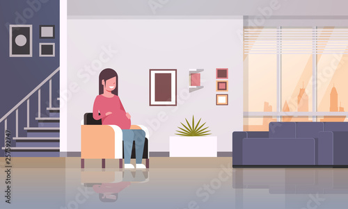 happy pregnant woman sitting in armchair girl holding her bump pregnancy and motherhood concept modern home living room interior flat full length horizontal