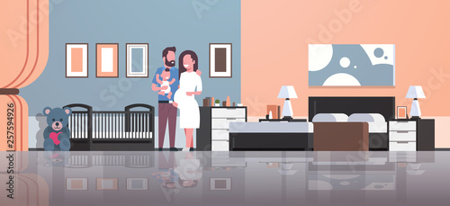 husband with pregnancy wife holding newborn baby son standing near crib happy family parenthood concept modern home bedroom interior flat full length