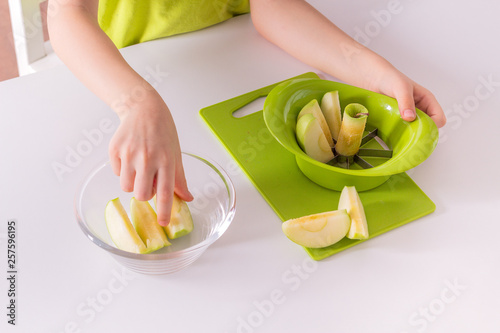 Children's hands are putting sliced apple into a bowl.