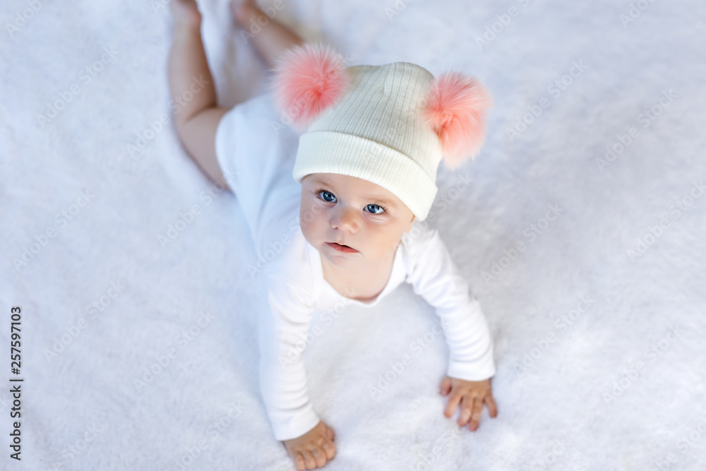 Cute adorable baby child with warm white and pink hat with cute bobbles. Happy baby girl learning crawl and looking at the camera. Close-up for xmas holiday and family concept Cute adorable baby child with warm white and pink hat with cute bobbles. Happy baby girl learning crawl and looking at the camera. Close-up for xmas holiday and family concept
