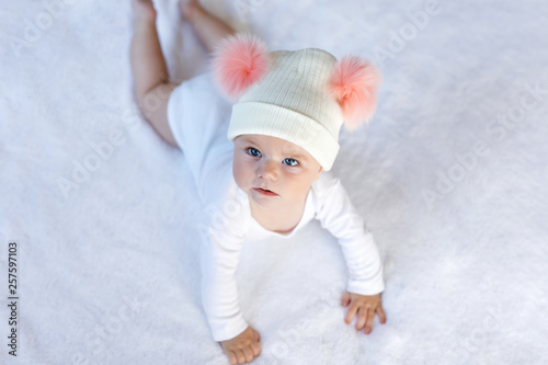 Cute adorable baby child with warm white and pink hat with cute bobbles. Happy baby girl learning crawl and looking at the camera. Close-up for xmas holiday and family concept