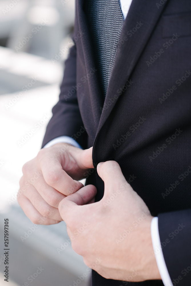 A man in a black suit fastens his jacket. Advertising of men's clothing.