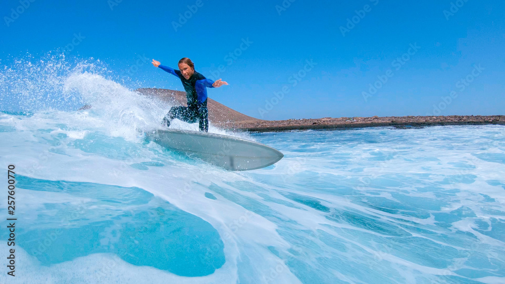 LOW ANGLE: Surfer guy carves a wave and splashes water at the camera.