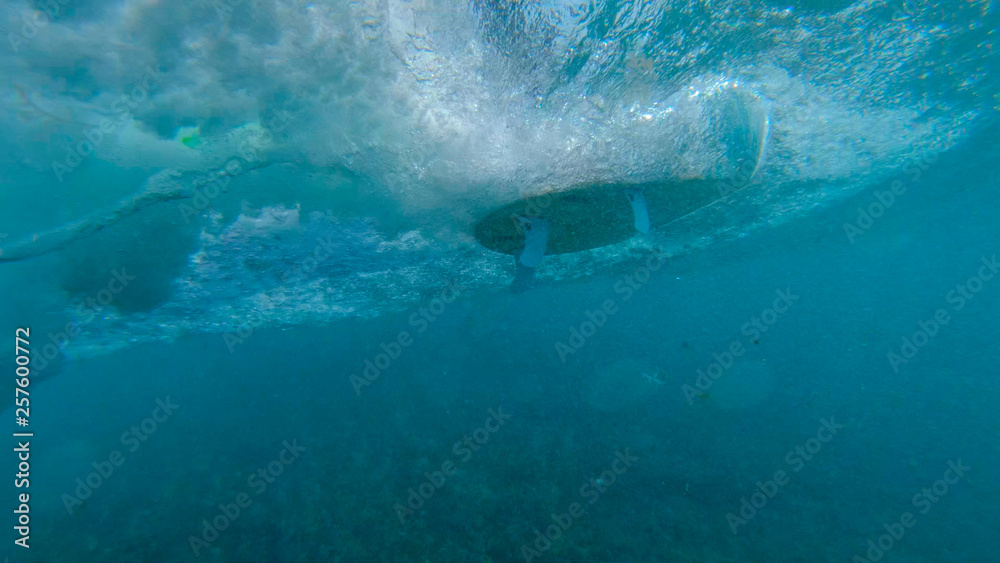 UNDERWATER: Unrecognizable surfer riding ocean waves on a new white surfboard