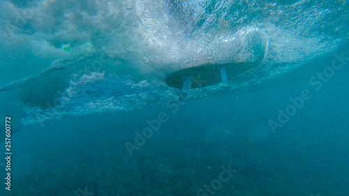 UNDERWATER: Unrecognizable surfer riding ocean waves on a new white surfboard