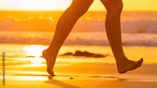 LOW ANGLE: Unrecognizable woman running barefoot on wet sand in the evening.