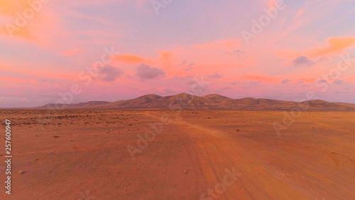 AERIAL: Flying towards large volcanic structure in pink colored desert sunset.