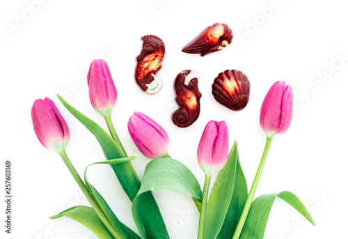 Belgian praline chocolate sweets and a pink delicate tulip flowers, isolated on white background. Spring holiday present concept.