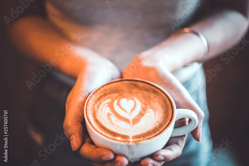 woman hold a cup of latte art coffee in hand at cafe, vintage tone 