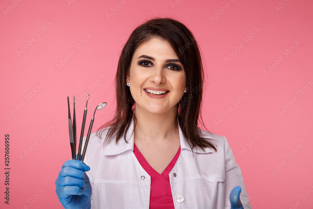 Pretty yong dentist in blue gloves with medical tool isolated over the pink background Pretty yong dentist in blue gloves with medical tool isolated over the pink background