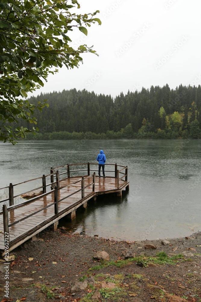 Fototapeta premium Young man wearing blue jacket enjoying the view of a mountain lake in winter. 