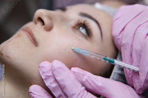 The doctor cosmetologist makes the Rejuvenating facial injections procedure for tightening and smoothing wrinkles on the face skin of a beautiful, young woman in a beauty salon.