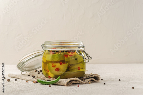 Fermented avocado vegetables with red chili peppers. Glass jar on a light background. Natural linen fabric. photo