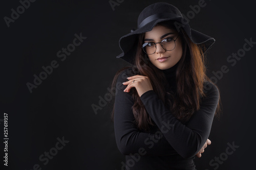 Brunette woman with long and shiny dark hair in a black Hat. Beautiful model on dark background. Studio photosession