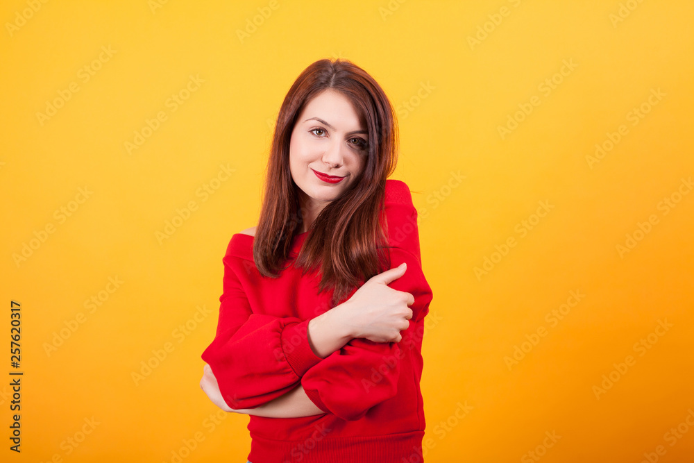Portrait of cute young woman gives herself a hug over yellow background Portrait of cute young woman gives herself a hug over yellow background