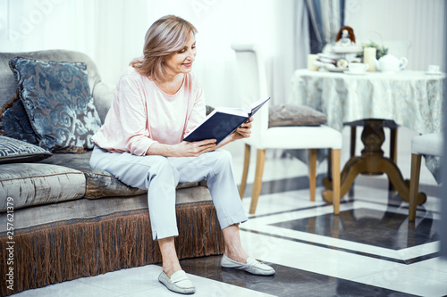 Middle Aged Woman Sitting On Sofa And Reading Bible