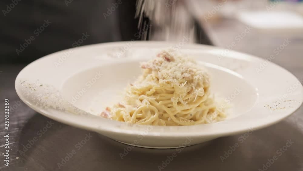 Close-up of adding parmesan in carbonara spaghetti in a plate ready to serve. Cook putting parmesan cheese in pasta with bacon into a serving plate in italian restaurant Close-up of adding parmesan in carbonara spaghetti in a plate ready to serve. Cook putting parmesan cheese in pasta with bacon into a serving plate in italian restaurant