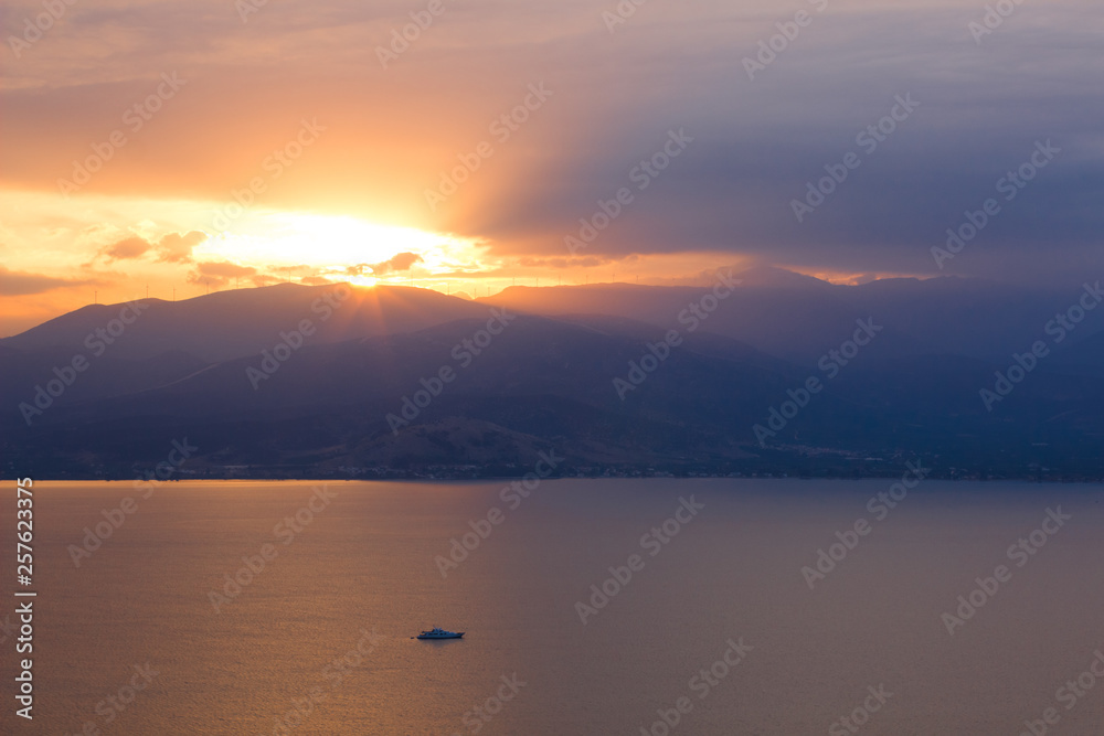 beautiful dramatic north scenery landscape with sunset and rays from mountain ridge silhouette above calm lake water surface and small yacht, daily planet travel photography