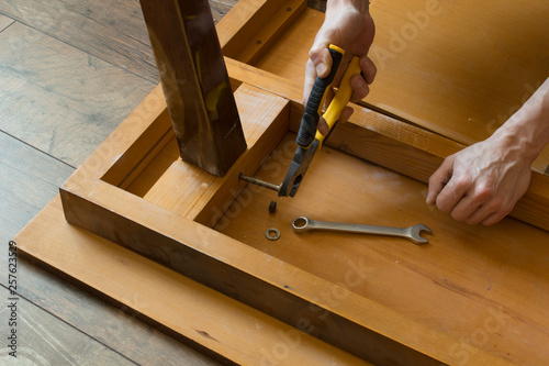 The hands of a carpenter restoring repairing wooden furniture with pliers tool, Close-up.