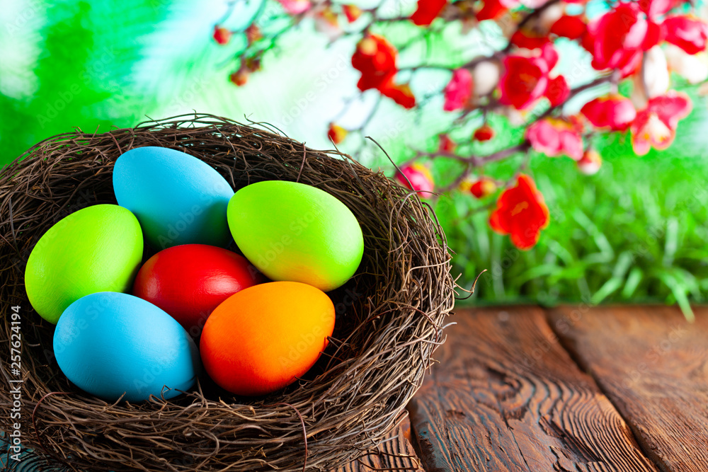 Colored Easter eggs in the nest on wooden table and springtime nature background Colored Easter eggs in the nest on wooden table and springtime nature background