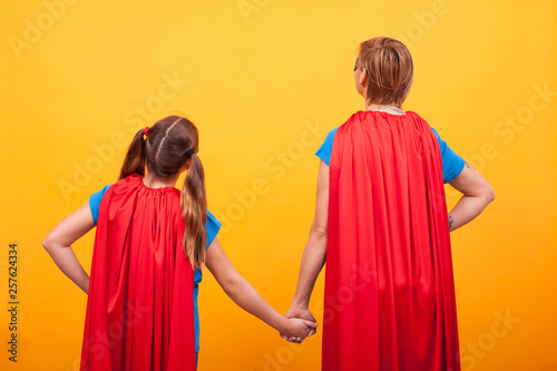 Back view of mother and her little girl dressed like superheros holding hands.