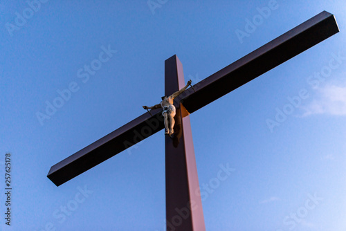 A big wooden cross with a statue of Jesus Christ in a cemetery, with a blue sky in the background.