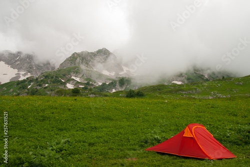 Red tourist tent is against mountains covered with clouds