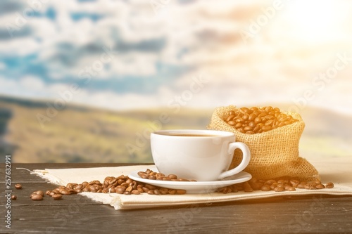 Cup of hot coffee with beans on background
