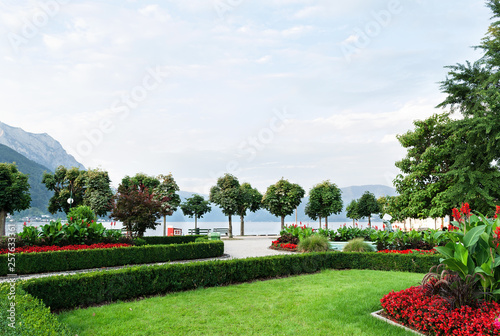 View of the mountains  the lake and the embankment of the city with trimmed trees  shrubs  lawn and flower beds.