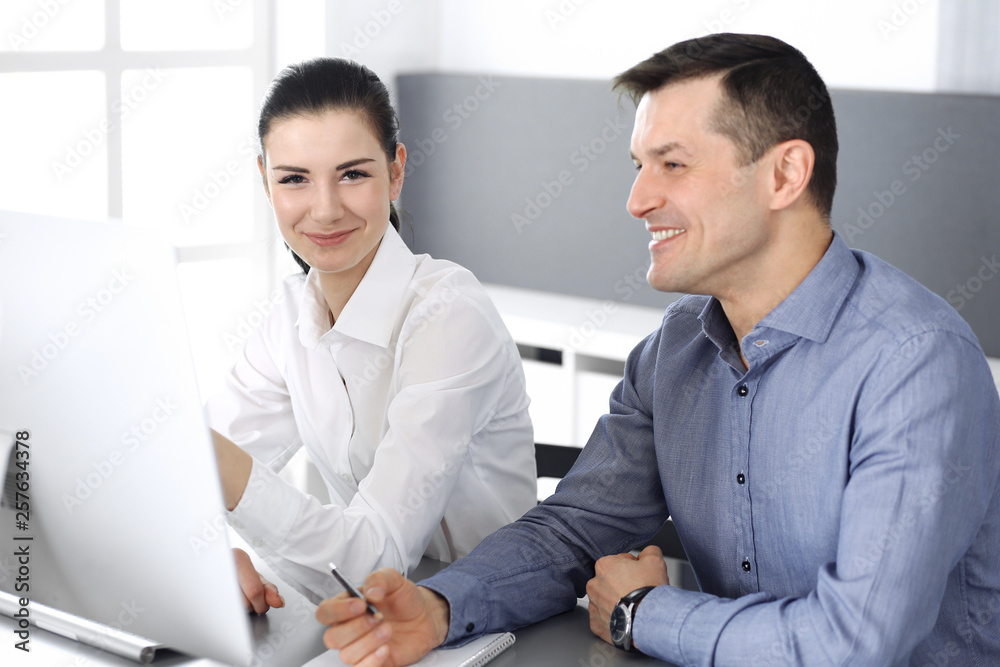 Cheerful smiling businessman and woman working with computer in modern office. Headshot at meeting or workplace. Teamwork, partnership and business concept Cheerful smiling businessman and woman working with computer in modern office. Headshot at meeting or workplace. Teamwork, partnership and business concept
