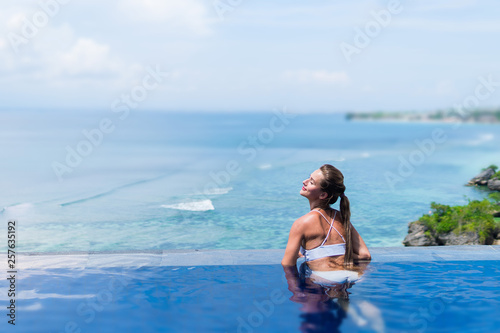 Young woman in white bikini enjoying a sun in the infinity pool. Vacations and summer concept