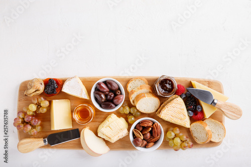 Cheese plate. French cheese with nuts, grape, berries, dried fruits and honey on cutting board on white. Camembert, Livarote, Pont-L'eveque cheese from Normandy and comte cheese. Top view. photo