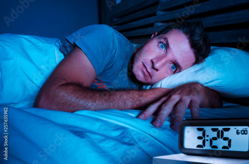 Fotografia restless worried young attractive man awake at night lying on bed sleepless with