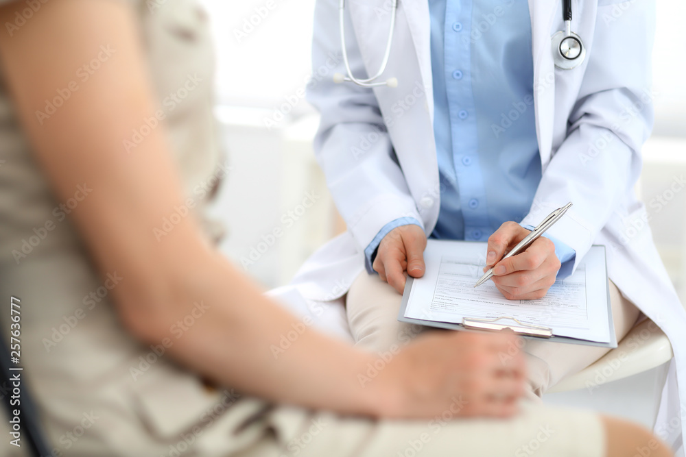 Doctor and patient talking. Physician at work in hospital while writing up medication history records form on clipboard near sitting woman. Healthcare and medicine concepts Doctor and patient talking. Physician at work in hospital while writing up medication history records form on clipboard near sitting woman. Healthcare and medicine concepts
