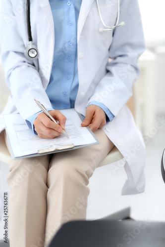 Female doctor writing up medication history records form on clipboard  while sitting at the chair. Physician at work in hospital or clinic. Healthcare  insurance and medicine concept