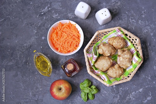 Ingredients for cooking vegetable salad: raw Jerusalem artichoke in wicker basket, raw grated carrots, apple, olive oil, red wine vinegar, fresh basil, salt, pepper. Top view. Copy space.