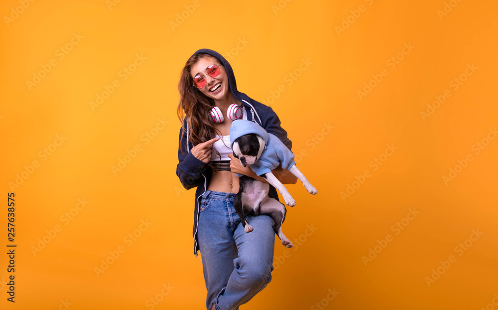 Obraz premium Charming, pretty girl with beaming smile and make up holding dog in hands near face, together looking at camera. portrait of cheerful fashion hipster girl going crazy in casual colorful hipster yellow